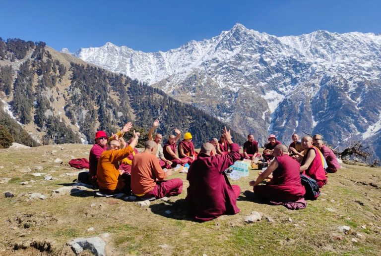 Visitors on a grassy ridge with the Dhauladhar mountains behind them