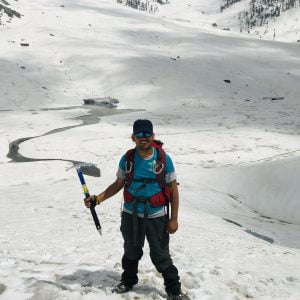 Trekker standing on a snowy mountain slope holding an ice axe during a winter trek in the Himalayas.