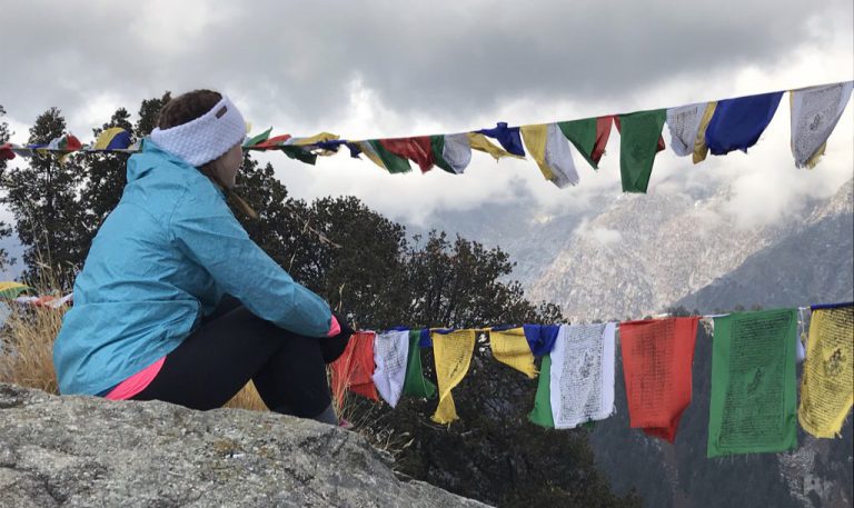 Traveller beside prayer flags overlooking the mountains