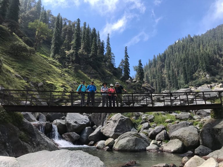 Hikers crossing a wooden bridge above a rocky stream